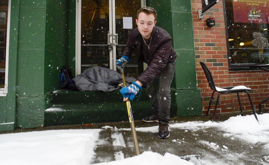 Mikey Reynolds, an employee at The Works on Main Street in Brattleboro, Vt., shovels the sidewalk in front of the restaurant as a person who is facing homelessness sleeps in a door entryway while seeking refuge from the snow storm on Saturday, March 23, 2024.