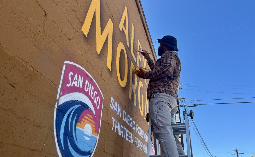 A man paints the lettering on a mural of soccer star Alex Morgan at Mike Hess Brewing in North Park, Sept. 5, 2025.