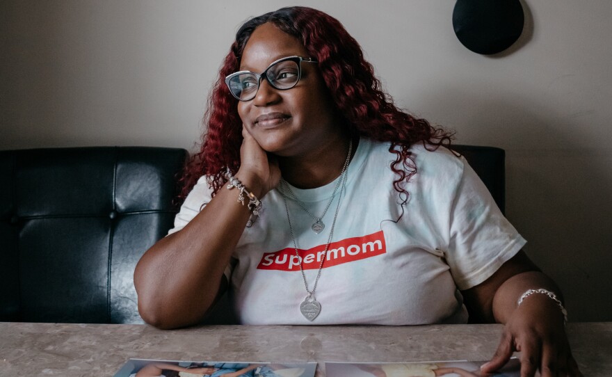 Cassie looks at family photos at her kitchen table. One is from when she was living in a transition home for women fleeing domestic violence, and more recent photos taken after her youngest daughter was born.