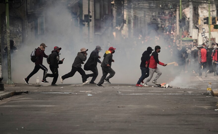 Demonstrators run across a street during an anti-government protest in La Paz, Bolivia, Monday, May 18, 2026.