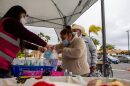 Lilian Serrano helps Maria Roja bag face masks and rapid COVID-19 tests outside of a vaccine clinic at La Mirada Academy in San Marcos, Calif. in this undated photo.