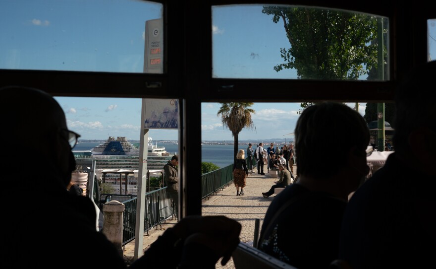 Passengers on Tram 28, a popular and scenic trolley, stare out at people gathered on the seaside in Lisbon, Portugal.
