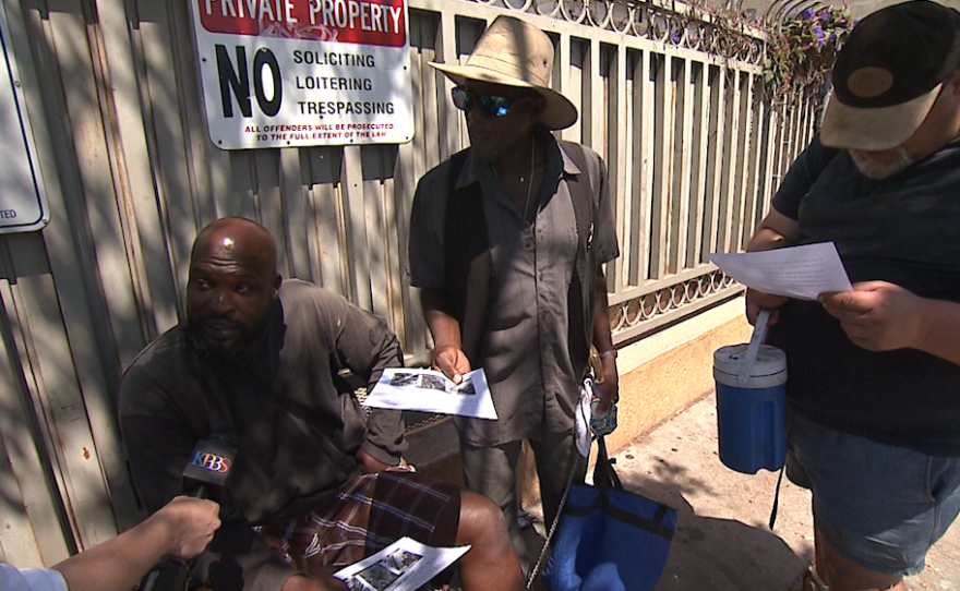 Richard Stevenson, left, and two other homeless men look at flyers showing photos of a man San Diego Police believe killed two homeless men and brutally assaulted two others, July 6, 2016.