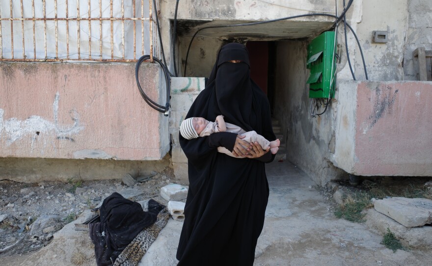 Mary, a Uyghur mother and the wife of a Uyghur commander in Syria, stands with her youngest child in front of their home.