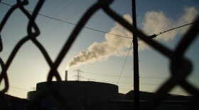 A factory chimney releases a long stream of smoke into the sky.