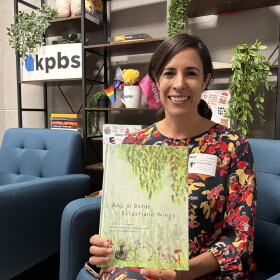 University of San Diego professor and founder of the Border Design Lab, Adriana Cuéllar, holds up her book, "Alas al Borde: Borderland Wings" in the KPBS social media studio, July 30, 2026.