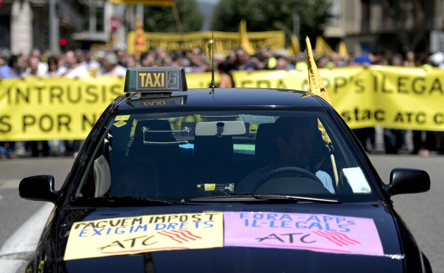 A taxi precedes demonstrators during a protest against Uber in Barcelona on Wednesday. A conventional taxi license in Spain can cost 137,000 euros ($185,400), making competition from services like Uber a major financial issue.
