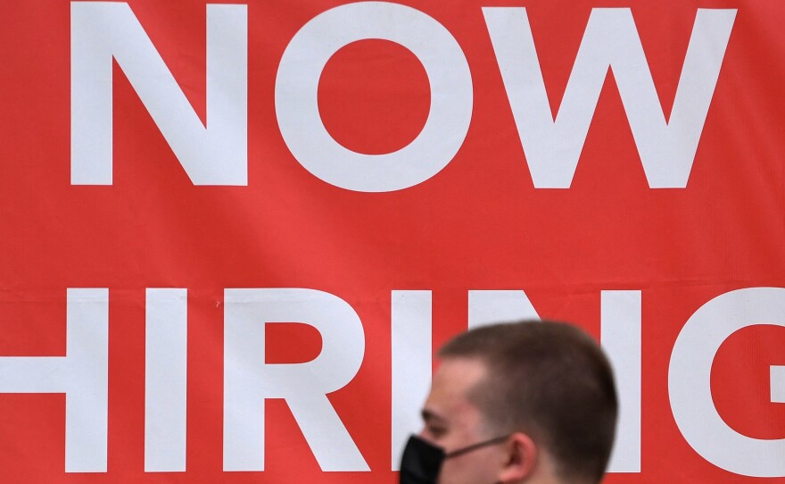 A man passes a "Now Hiring" sign outside a store this month in Arlington, Va. The Fed chairman noted Friday that more progress needs to be made to return to full employment.