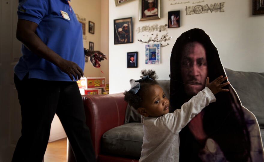 Khy Franklin, 1, plays with a life-size cutout poster of her father, Kent Franklin, who was shot and killed on July 18, 2016. He was 21. His mother, Tracy Williams, (left) lost both of her twin sons to gun violence. Keith Franklin died in an accidental shooting in 2007 when he was 12. This cutout is kept by one of Kent's friends, but Tracy said she had another poster of her son.