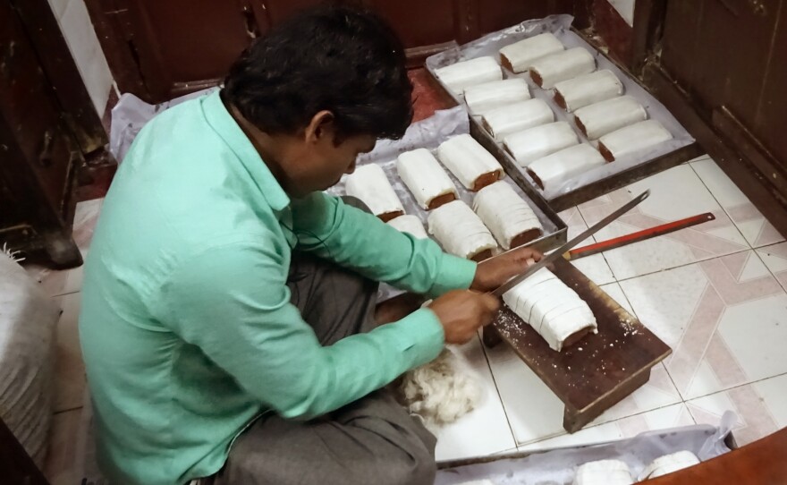 A worker slices rich fruitcake with almond icing at the family-run Saldanha Bakery.