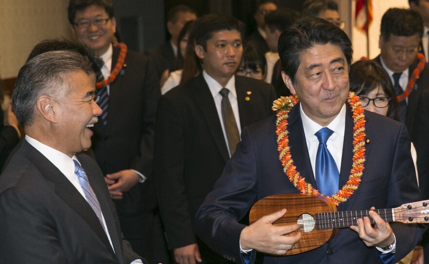 Japanese Prime Minister Shinzo Abe (right), strums a pineapple-shaped ukulele presented to him by Hawaii Gov. David Ige at a dinner on Monday in Honolulu. Abe and President Obama visited Pearl Harbor on Tuesday, 75 years after the surprise Japanese attack that drew the U.S. into World War II.