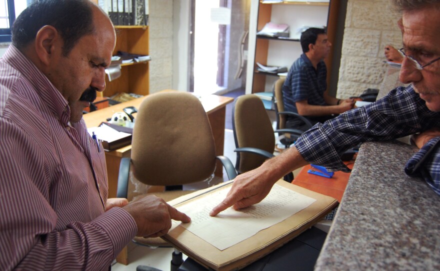A government clerk in Ramallah helps a Palestinian man look up 1935 property tax records showing his family name. Handwritten ledgers from the times of Ottoman, British and Jordanian rule are still used to help determine Palestinian land ownership.