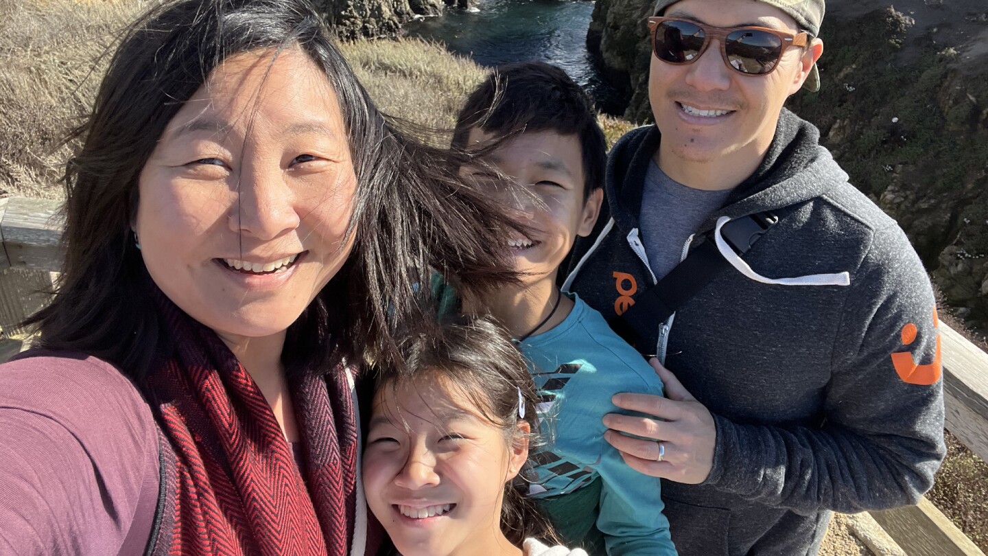 A smiling family looking windswept poses in front of a scenic ocean view.