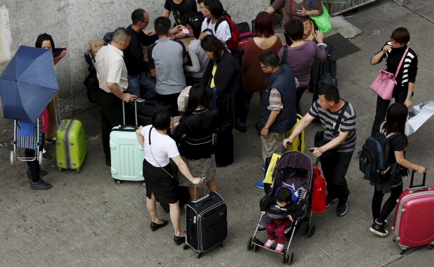 A man pushing a stroller passes parallel traders in Hong Kong distributing goods to be brought into Shenzhen, China, on Monday. China said it will limit the number of visits that residents of Shenzhen can make to Hong Kong. The move is an attempt to ease the flow of mainland visitors in the former British colony.