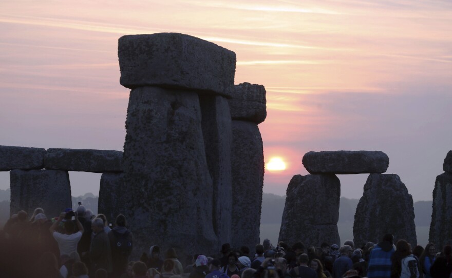Thousands of people stand among the ancient stones at Stonehenge in Salisbury, England, at sunrise on the summer solstice. Archaeologists on Monday announced the discovery of a ring of shafts about 2 miles away.