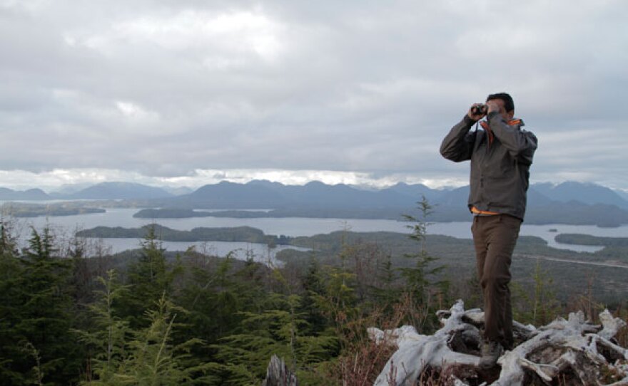 M. Sanjayan stands on mountain with binoculars in the Great Bear Rainforest.