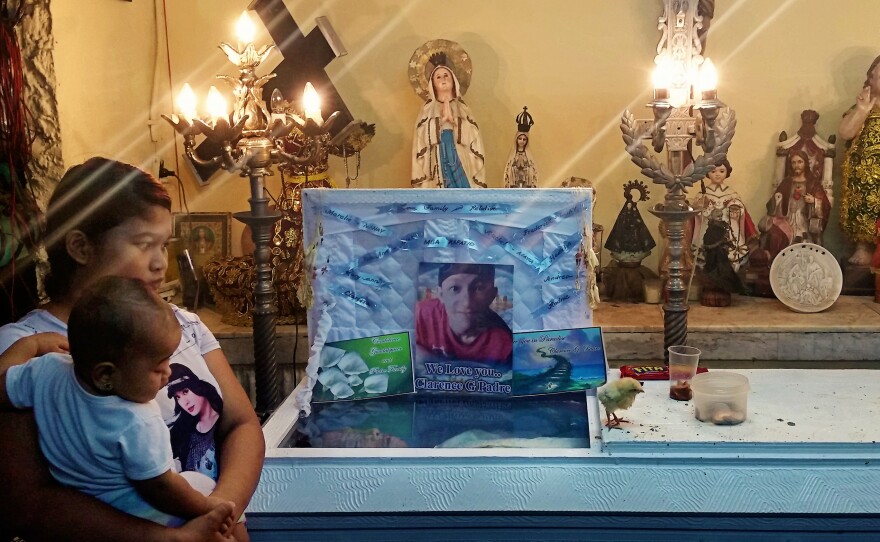 Clarence Jepadre's girlfriend Rachel Quebec stands with daughter Roseann in front of his casket. A chick paces on the coffin's lid. Jepadre, 17, was found stabbed to death. It's a tradition to place chicks on the coffins of murder victims to peck at the conscience of the killer.