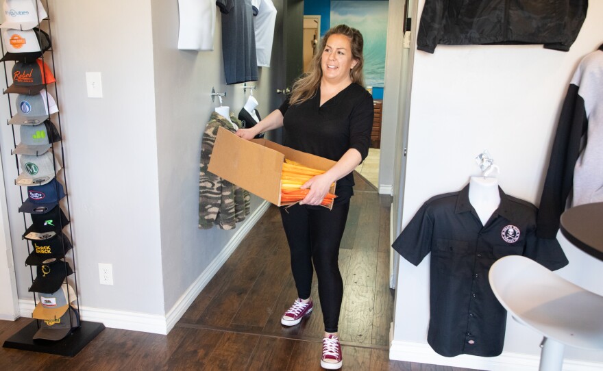 Heather Treviño carries a box of bandanas through the offices of Planet Apparel in San Diego on March 26, 2020.