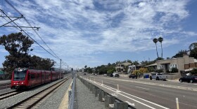 A Blue Line trolley passes by single-family homes in Bay Park, Aug. 25, 2025.