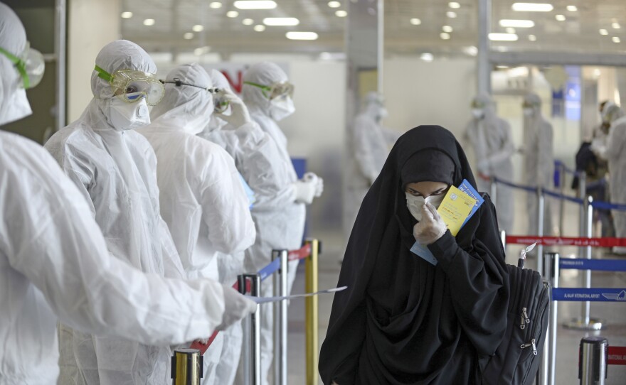 Staff in protective gear hand out information sheets about COVID-19 to Iraqi passengers returning from Iran at Najaf International Airport on March 5, 2020. Iraq was then experiencing a serious outbreak.