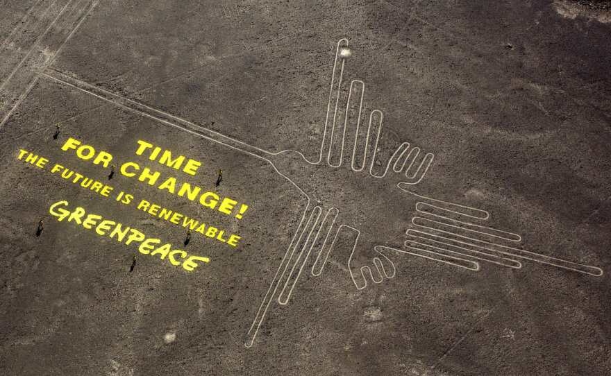 Greenpeace activists stand next to massive cloth letters next to the hummingbird geoglyph at Peru's sacred Nazca lines. The Peruvian government is pursuing criminal charges against the activists.