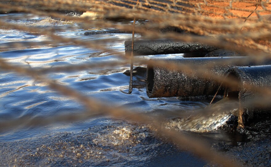 Dirty water from the oil wells flows through oil-caked pipes into a settling pit where trucks vacuum off the oil. A net covers the pit to keep out birds and other wildlife. Streams of this wastewater flow through the reservation and join natural creeks and rivers.