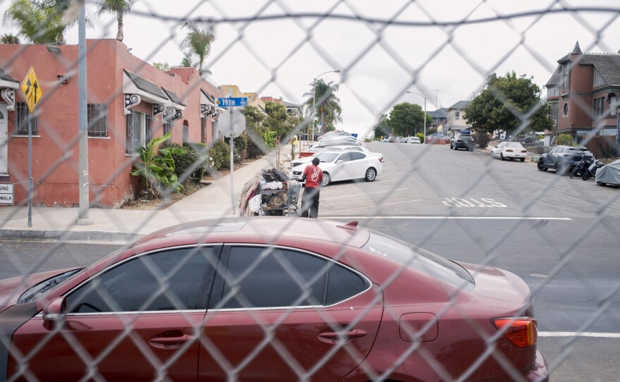 A man transports his belongings in a shopping cart on the city's side of a chain link fence in San Diego on Friday, Aug. 15, 2025.
