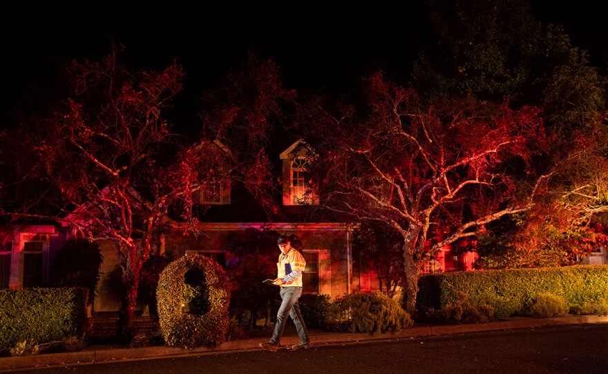 A Pacific Gas & Electric worker passes a home on Merrill Dr. in Moraga, Calif., as firefighters work to contain a wildfire burning behind it on Thursday, Oct. 10, 2019.
