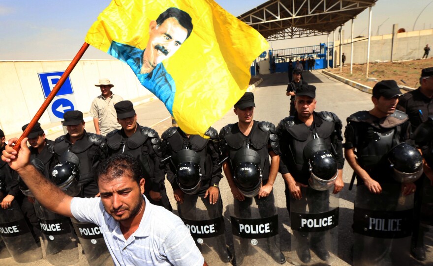 The U.S. has different policies toward different Kurdish groups. The U.S. works closely with Iraqi Kurds, whose policemen form a line in this photo. But the U.S. labels a militant Kurdish group from Turkey, the PKK, a terrorist organization. A PKK supporter waves a yellow flag of the group's leader. Three separate Kurdish militias have been fighting the group that calls itself the Islamic State.