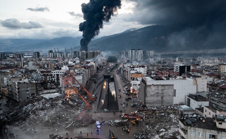 Smoke billows from the Iskenderun Port as rescue workers search the site of a collapsed building in Iskenderun, Turkey on Tuesday. The quakes caused widespread destruction in southern Turkey and northern Syria and were felt in nearby countries.
