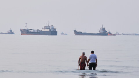Two men wade in the waters of the Strait of Hormuz with vessels anchored in the background, off Bandar Abbas, Iran, Sunday, July 12, 2026.