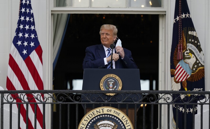 President Donald Trump removes his face mask to speak to a crowd of supporters from the Blue Room Balcony of the White House. Oct. 10, 2020.