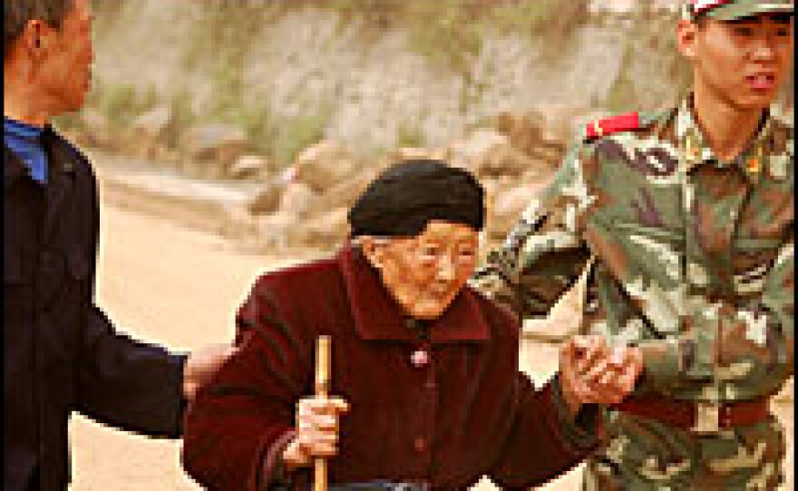 An elderly woman from a remote village near Dujiangyan is helped toward food and water.