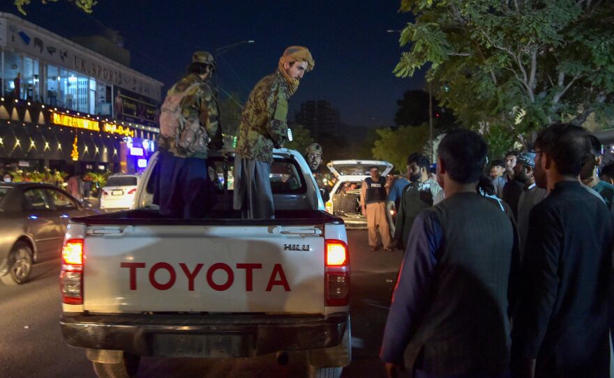 Taliban fighters stand on a pickup truck outside a hospital as volunteers bring injured people for treatment after two powerful explosions outside the airport in Kabul.