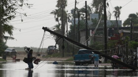 A man carries items through floodwater past downed electric lines after the passing of Hurricane Polo in Puerto San Carlos, Baja California Sur state, Mexico, Tuesday, Sept. 29, 2026.