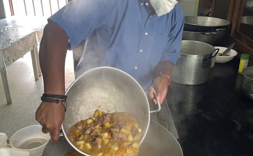 A cook pours beef stew into a large container for distribution to malnourished people.