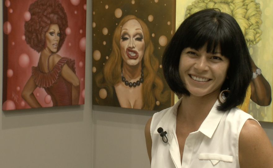 Artist Margaret Chiaro in front of a few of her rainbow series of portraits of drag queens.