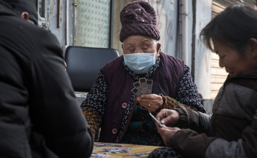 People play a game of cards outdoors. Wuhan's government has forbidden large gatherings.