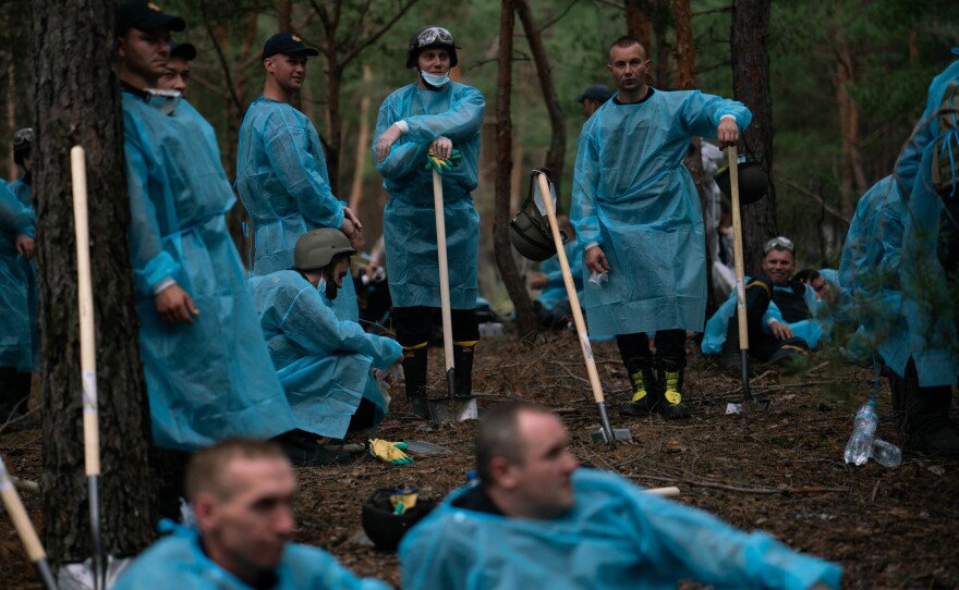Ukrainian investigators gather while they exhume bodies from a mass grave site in Izium on Friday.