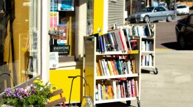 Libélula Books pictured from the sidewalk, with a yellow door and two carts of books outside.