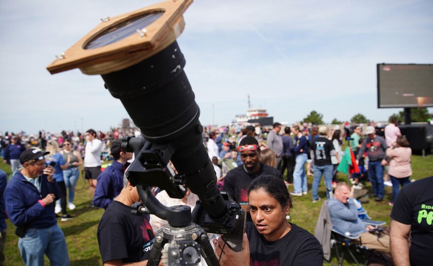 Indira Poovambur, of North Olmsted, Ohio, attempts to take a photo of the sun via the LCD screen of a camera with a telephoto lens outside the Great Lakes Science Center in Cleveland.