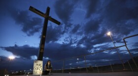 A woman sits next to a sign with a message that reads: ¨No More Guns! Make Love,¨in Juarez, Mexico,  where people are gathering for a vigil for the 3 Mexican nationals who were killed in an El Paso shopping-complex shooting, Aug. 3, 2019.