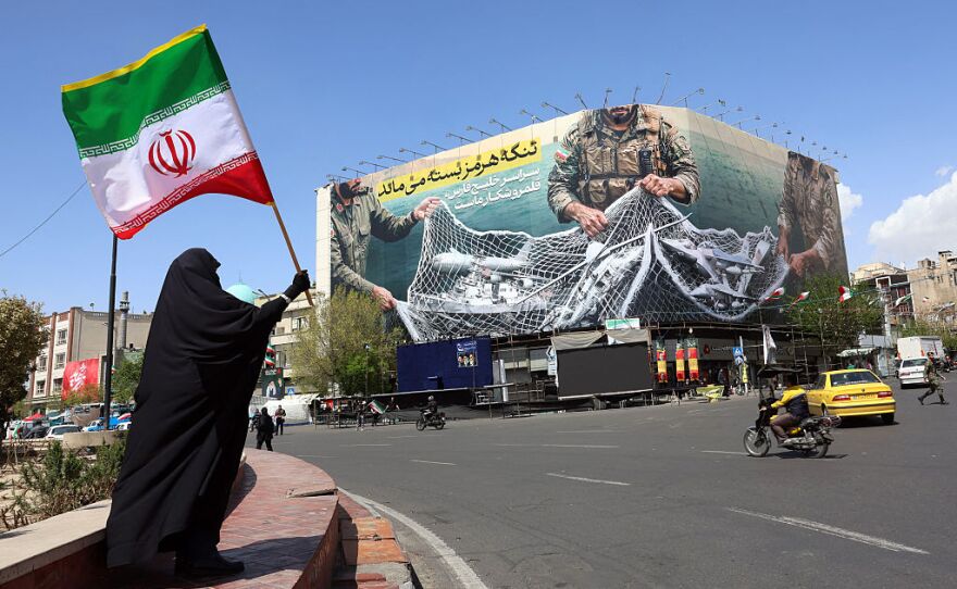 TOPSHOT - 5 Nisan 2026'da Tahran'daki Enkaleb Meydanı'nda, üzerinde 'Hürmüz Boğazı kapalı kalmaya devam ediyor' yazan bir panonun yanında duran bir kadın, İran ulusal bayrağını tutuyor.