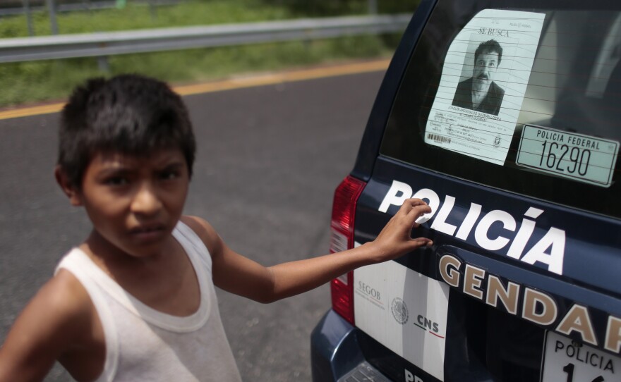 A boy stands next to a police car with a picture of fugitive drug lord Joaquin "El Chapo" Guzman's at a checkpoint on the highway connecting Mexico City and Acapulco, in Guerrero State, Mexico.