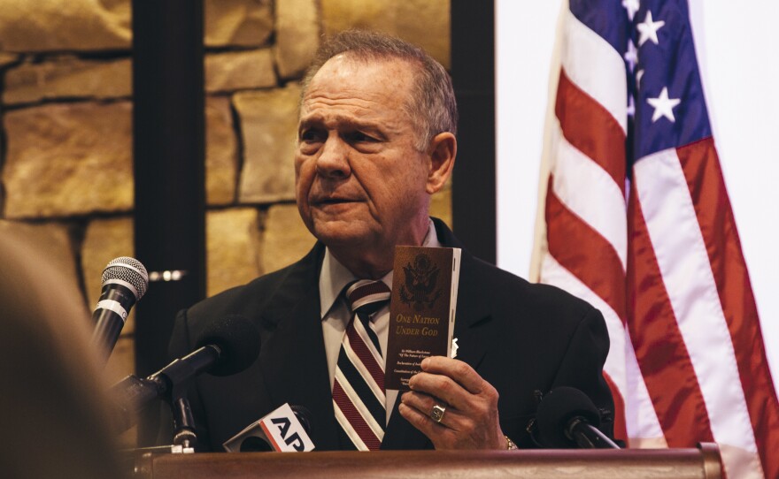 Republican Senate candidate Roy Moore has been accused of sexual misconduct by multiple women, some of whom were teenagers at the time. He holds up a copy of his handbook, <em>One Nation Under God.</em>