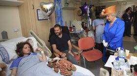 Britain's Queen Elizabeth II, right, speaks to Evie Mills, 14, from Harrogate, and her father Craig, as she visits the Royal Manchester Children's Hospital in Manchester England, to meet victims of the terror attack in the city earlier this week and to thank members of staff who treated them Thursday May 25, 2017.