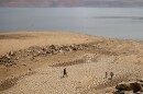 In this Aug. 22, 2021, file photo, a family walks over cracked mud near Lake Oroville's shore as water levels remain low due to continuing drought conditions in Oroville, Calif.