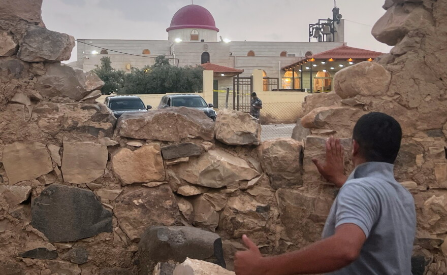 A man looks through a gap in a stone wall toward a Greek Orthodox church where gunmen opened fire during a funeral hours earlier in Hamoud village, in Jordan's Karak governorate on Friday.