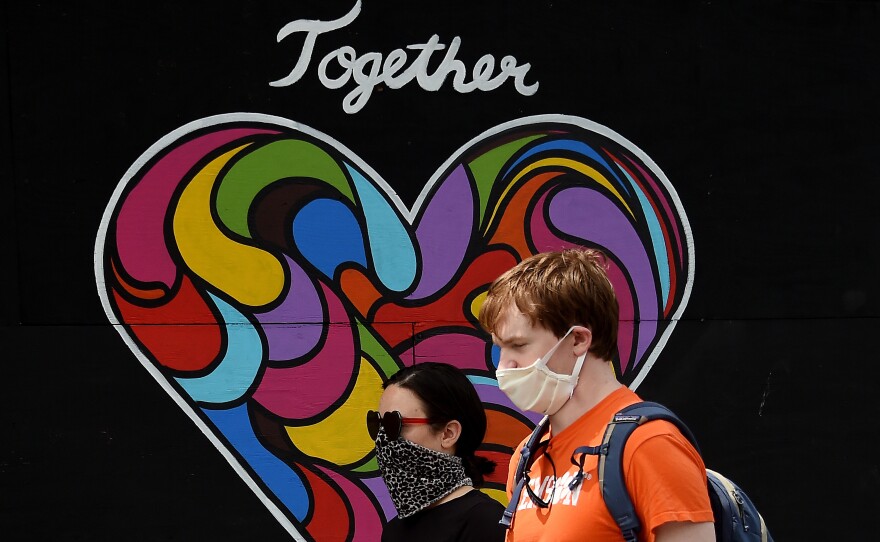 People wearing masks walk past a mural of encouragement displayed outside a store amid the coronavirus pandemic on Tuesday in Washington, D.C.