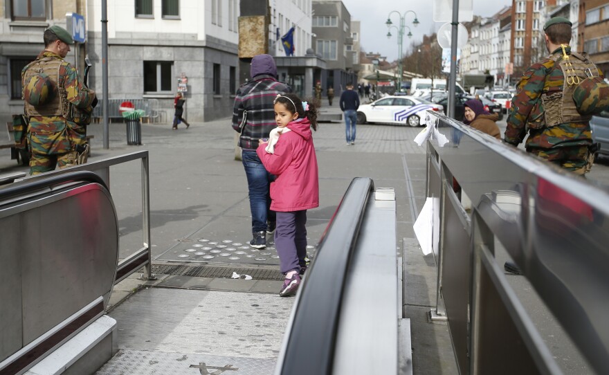 A child looks back down the exit from the subway as two soldiers stand watch. While the Brussels airport remains closed, some subways stops have reopened.